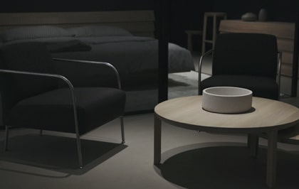 A set of two dark chairs and a table in a room with a bed behind them